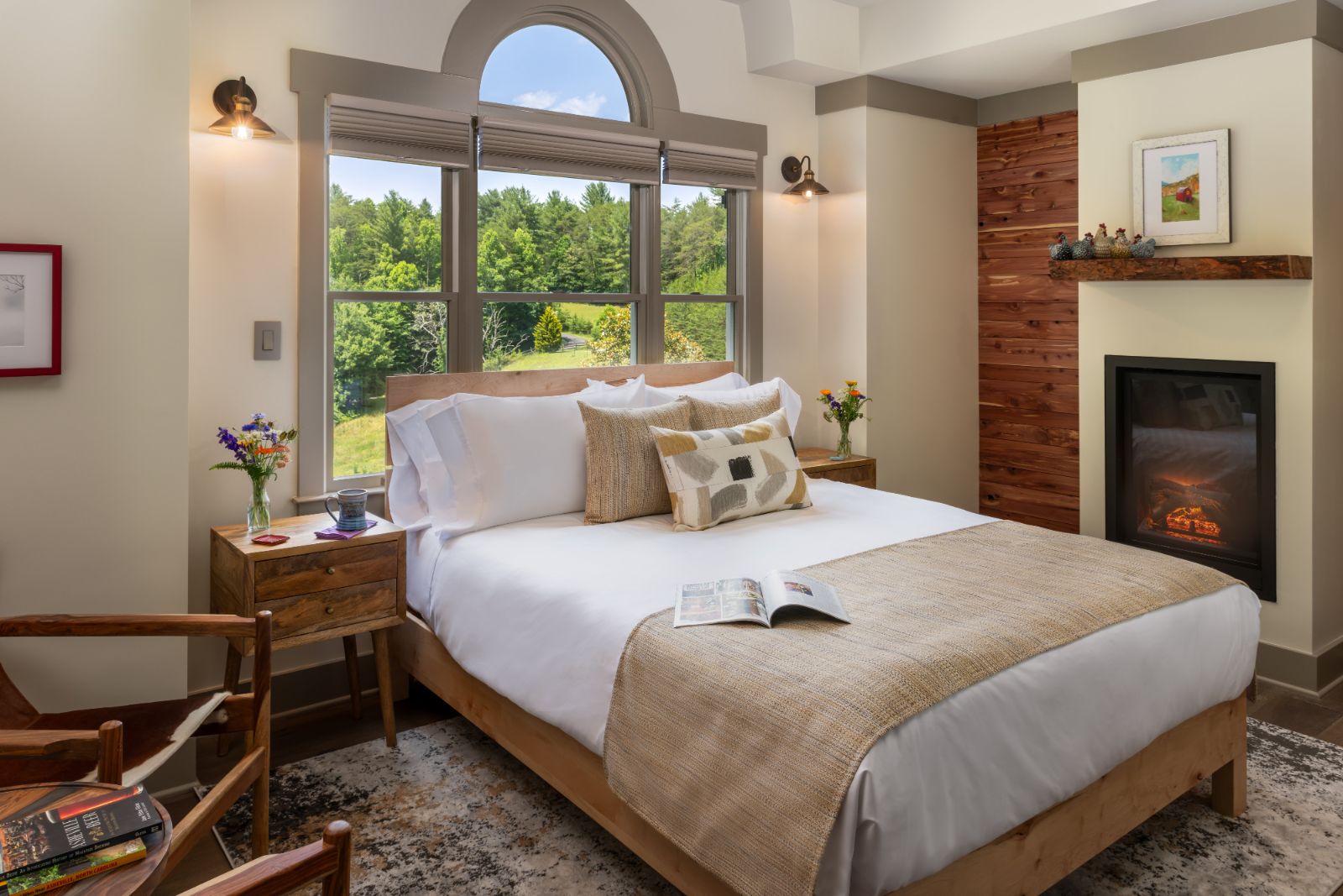Guest room with a lit fireplace, cedar accent wall, and an arched window looking out on the farm at Inn at Amaris Farms in Weaverville, NC